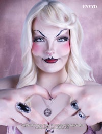 a woman with makeup on her face making a heart sign